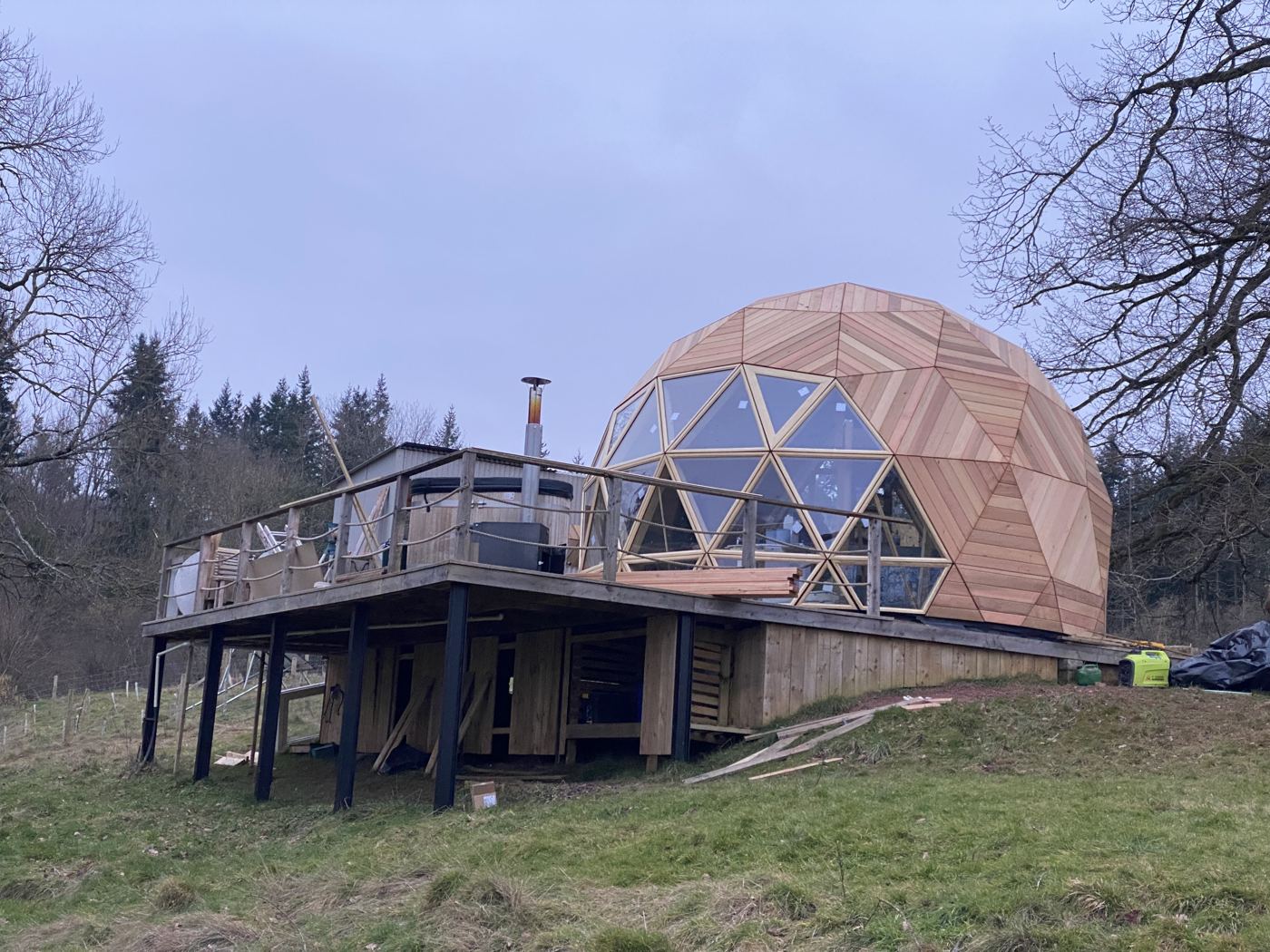 The Fold — cedar-clad Wilder dome with full-height glazing on a raised deck with hot tub, woodland behind