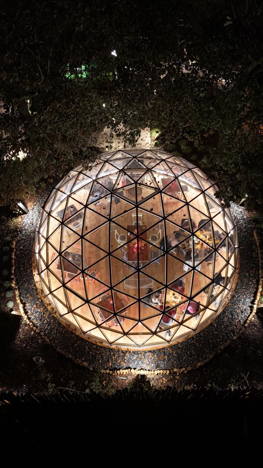 Overhead night view of a glowing Wilder glazed dome, guests dining inside beneath the trees